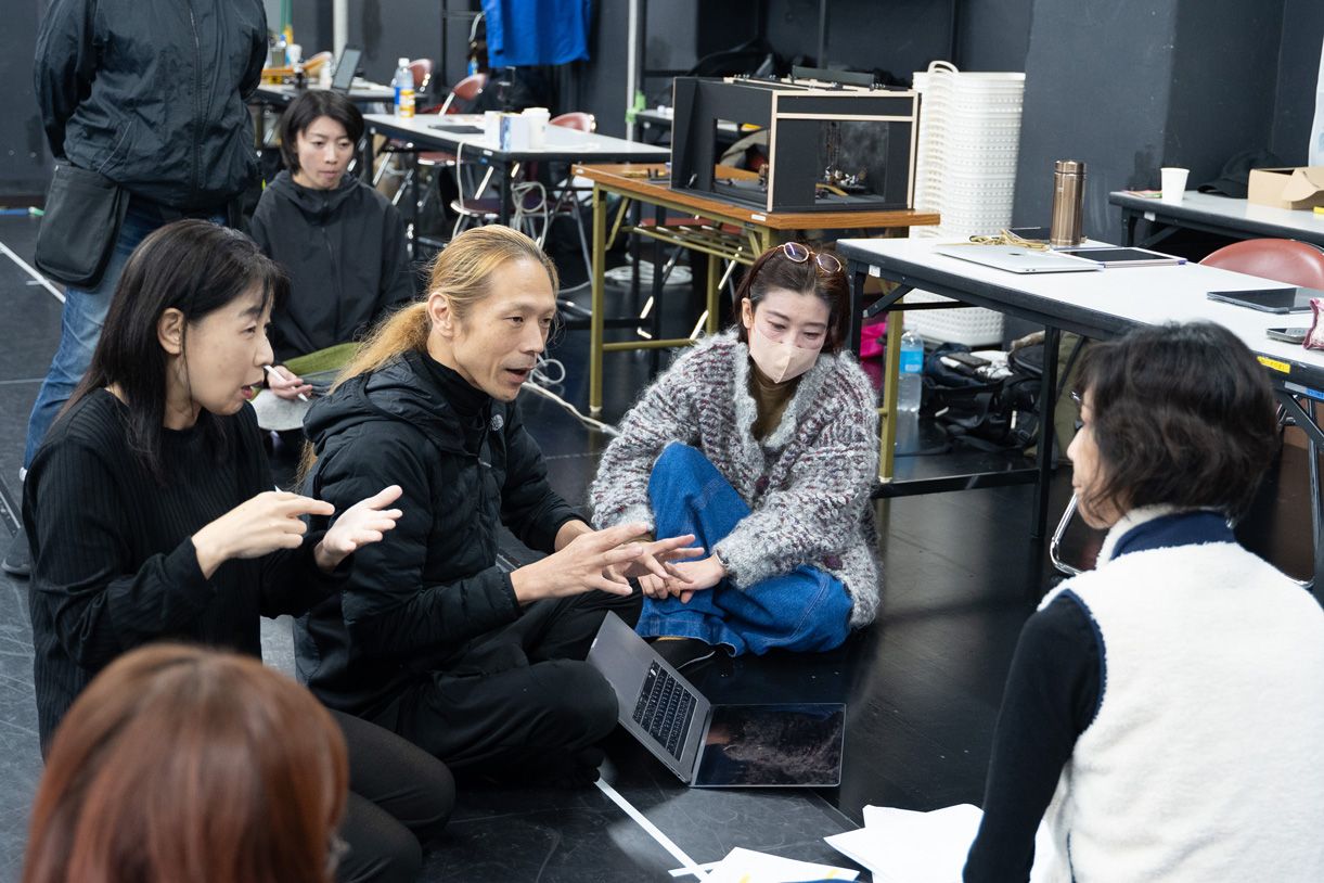 稽古場で床に座って話す、4-5人の姿。