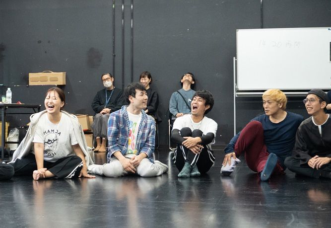 複数のキャストが稽古着で床に座っている